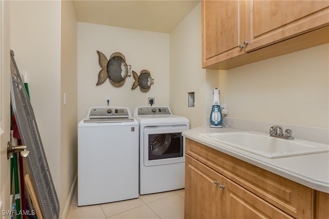 clothes washing area with sink, washing machine and dryer, cabinets, and light tile patterned floors