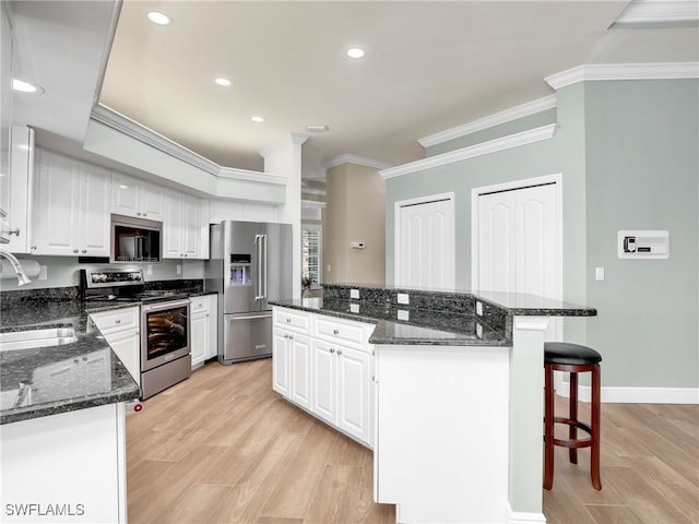 kitchen with white cabinets, dark stone counters, appliances with stainless steel finishes, and light hardwood / wood-style floors