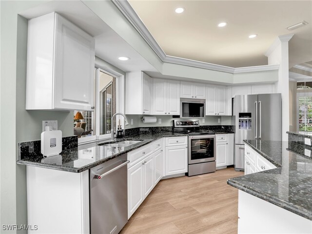 kitchen with appliances with stainless steel finishes, light hardwood / wood-style floors, sink, white cabinets, and dark stone counters