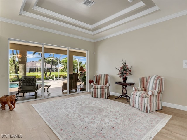 living area with a raised ceiling, ornamental molding, and light wood-type flooring