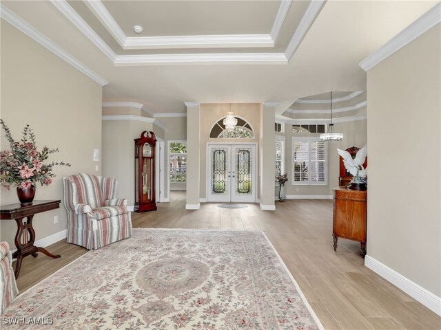 foyer entrance with light hardwood / wood-style floors, french doors, crown molding, a tray ceiling, and a notable chandelier