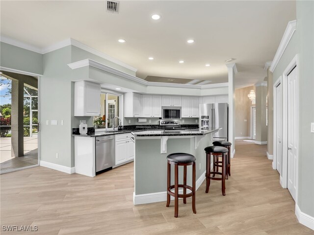 kitchen with stainless steel appliances, white cabinetry, crown molding, light wood-type flooring, and a kitchen breakfast bar