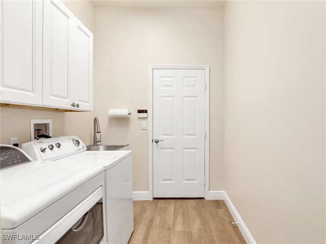 laundry room featuring sink, washing machine and clothes dryer, light hardwood / wood-style floors, and cabinets