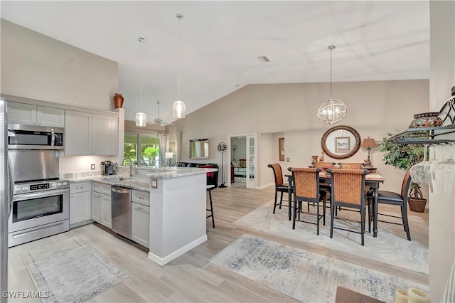 kitchen featuring appliances with stainless steel finishes, a notable chandelier, light wood-type flooring, light stone counters, and decorative light fixtures