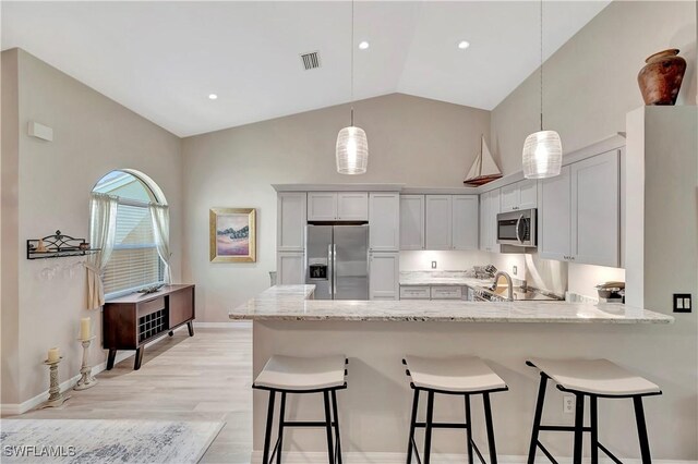 kitchen featuring pendant lighting, stainless steel appliances, white cabinetry, light hardwood / wood-style flooring, and a kitchen bar