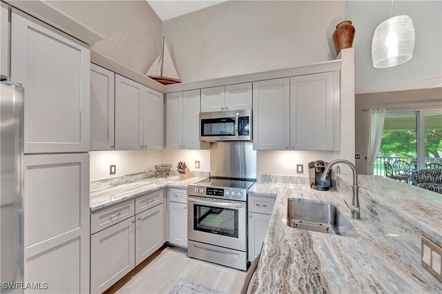 kitchen with appliances with stainless steel finishes, sink, pendant lighting, and light stone counters