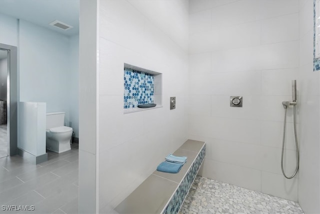 bathroom with tile patterned flooring, toilet, and tiled shower