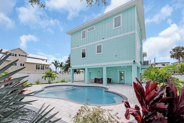 rear view of house with a fenced in pool, fence, board and batten siding, and a patio