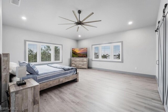 bedroom with ceiling fan, a barn door, and light hardwood / wood-style flooring