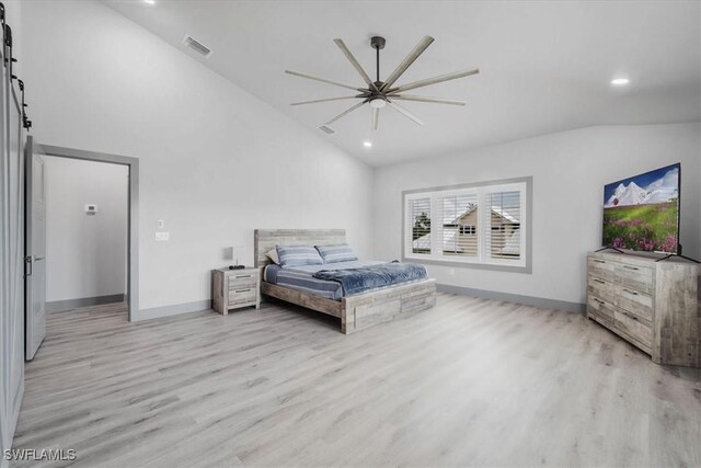 bedroom with a barn door, ceiling fan, vaulted ceiling, and light wood-type flooring