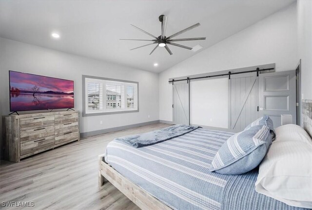 bedroom with a barn door, ceiling fan, light hardwood / wood-style floors, and lofted ceiling