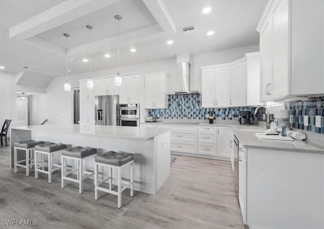 kitchen featuring white cabinets, a kitchen island, wall chimney range hood, and stainless steel appliances