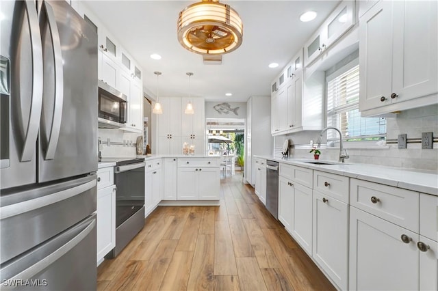 kitchen featuring sink, hanging light fixtures, stainless steel appliances, light hardwood / wood-style floors, and white cabinets