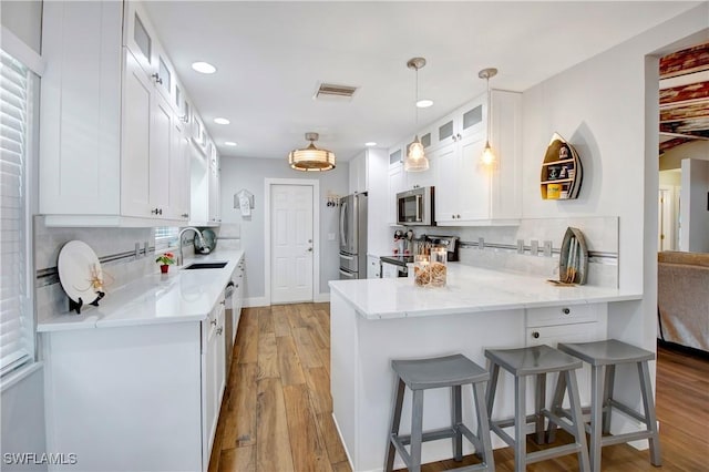 kitchen featuring white cabinetry, stainless steel appliances, light stone counters, kitchen peninsula, and light wood-type flooring