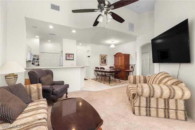 carpeted living room with ceiling fan and a high ceiling