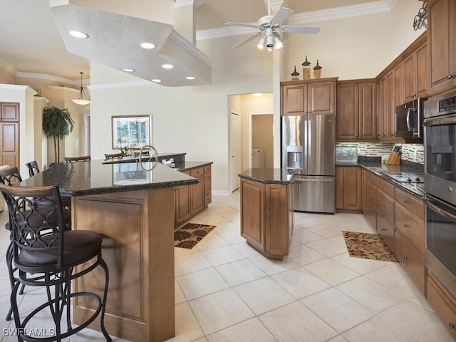 kitchen with a kitchen island with sink, appliances with stainless steel finishes, brown cabinetry, and ornamental molding