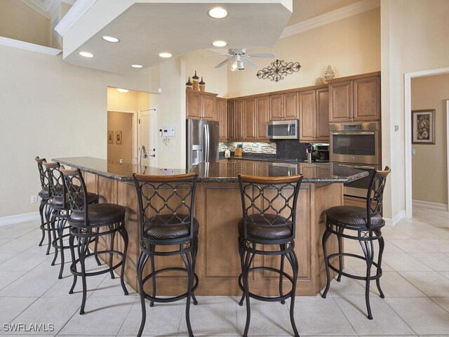 kitchen with a large island, ceiling fan, appliances with stainless steel finishes, light tile patterned flooring, and a breakfast bar area