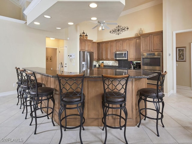 kitchen featuring appliances with stainless steel finishes, brown cabinetry, a breakfast bar area, and a large island with sink