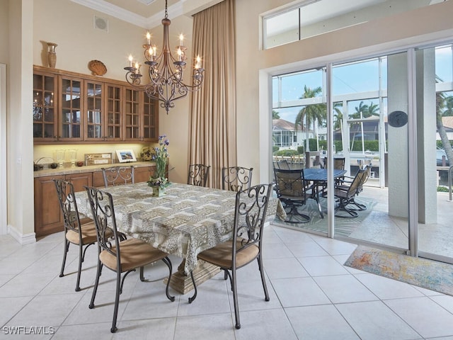 dining room with visible vents, a towering ceiling, an inviting chandelier, crown molding, and light tile patterned flooring