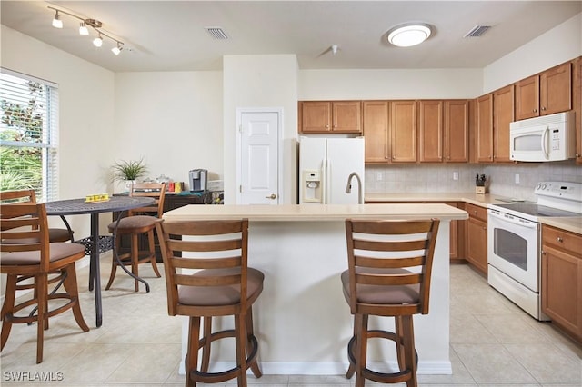 kitchen with white appliances, visible vents, brown cabinetry, a kitchen island with sink, and light countertops