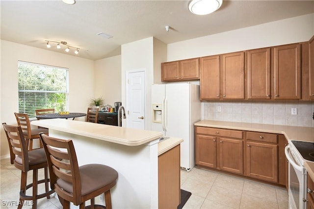 kitchen featuring brown cabinetry, a breakfast bar, white appliances, and light countertops