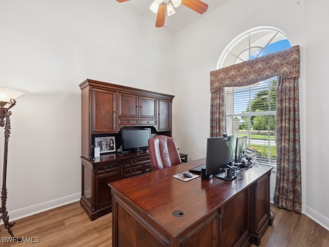 office featuring a towering ceiling, light hardwood / wood-style flooring, and ceiling fan