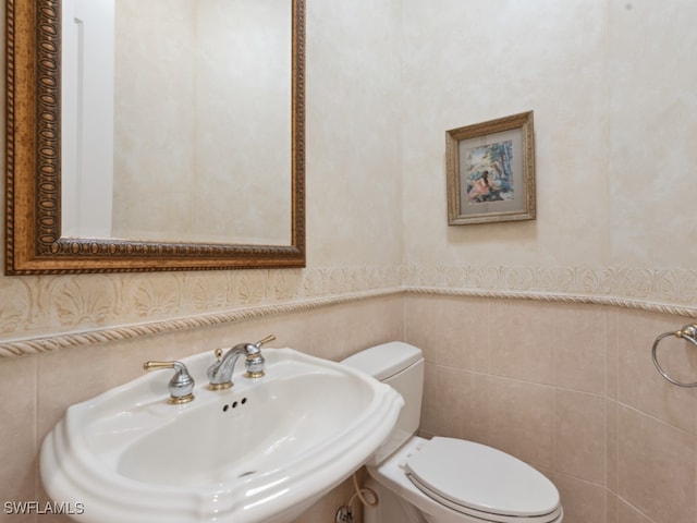 bathroom featuring sink, tile walls, and toilet