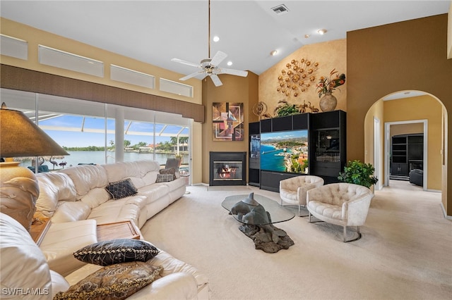 carpeted living room with visible vents, arched walkways, a glass covered fireplace, high vaulted ceiling, and a ceiling fan