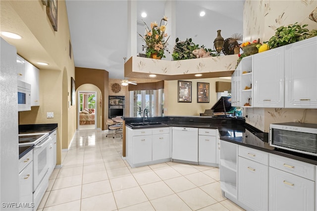 kitchen featuring kitchen peninsula, white appliances, sink, a high ceiling, and white cabinetry