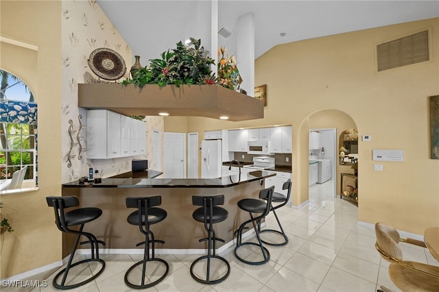 kitchen featuring white appliances, visible vents, a peninsula, arched walkways, and dark countertops