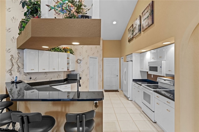 kitchen featuring a kitchen breakfast bar, white appliances, vaulted ceiling, light tile patterned floors, and white cabinets