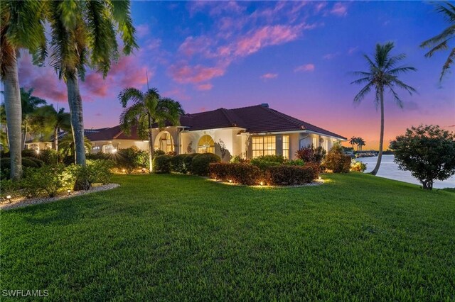 property exterior at dusk featuring a lawn and a water view