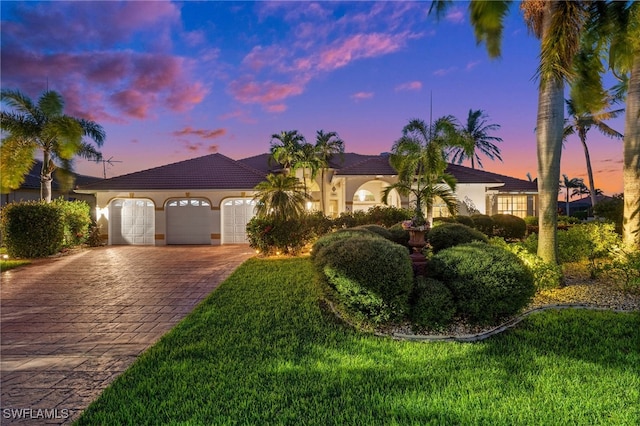 mediterranean / spanish house with a tiled roof, stucco siding, decorative driveway, a yard, and an attached garage