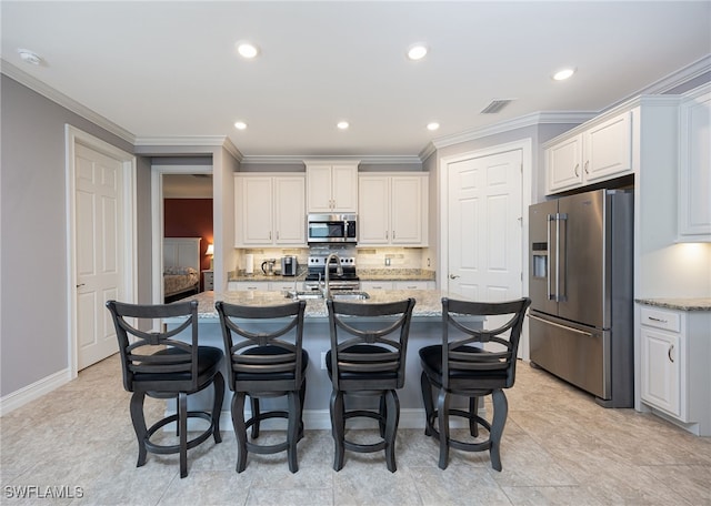 kitchen with light stone countertops, a kitchen island with sink, stainless steel appliances, and tasteful backsplash