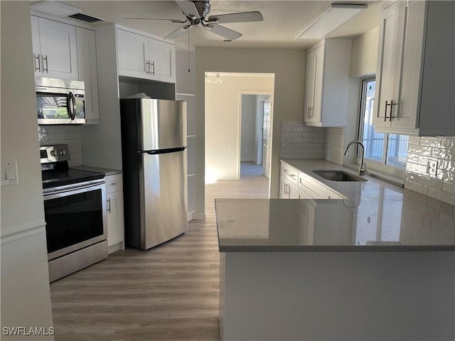 kitchen with stainless steel appliances, a peninsula, a sink, light wood-style floors, and white cabinets