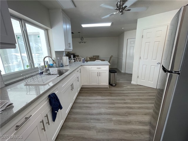 kitchen featuring hardwood / wood-style floors, white cabinetry, light stone counters, stainless steel refrigerator, and ceiling fan