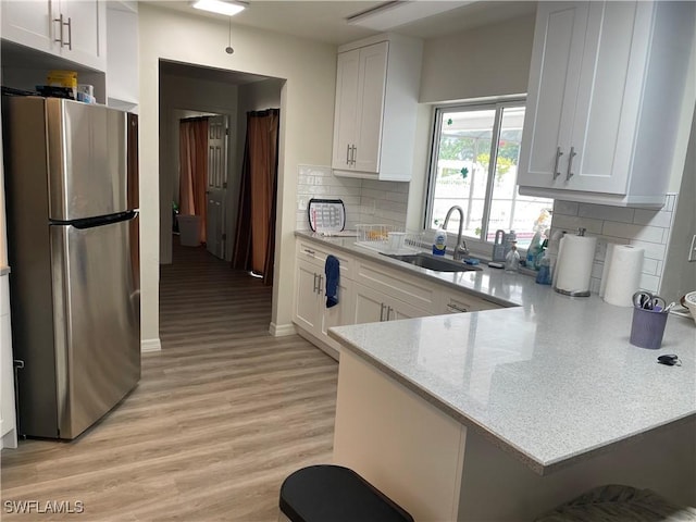 kitchen featuring light stone counters, a sink, freestanding refrigerator, and white cabinets