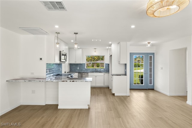 kitchen with stainless steel appliances, light wood-type flooring, tasteful backsplash, white cabinetry, and kitchen peninsula