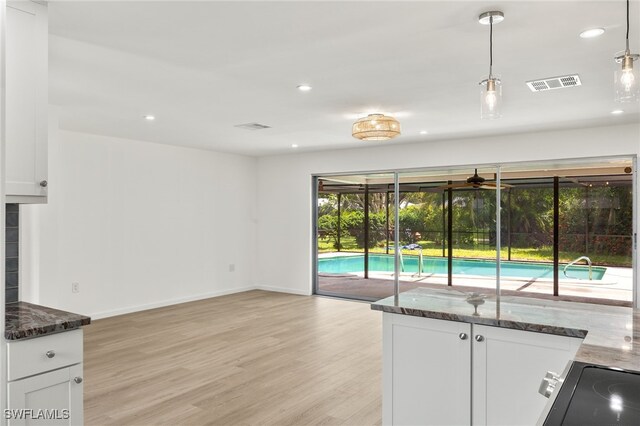 kitchen with light wood-type flooring, decorative light fixtures, white cabinetry, and dark stone counters