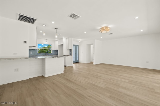 kitchen with backsplash, white cabinets, light wood-type flooring, and decorative light fixtures