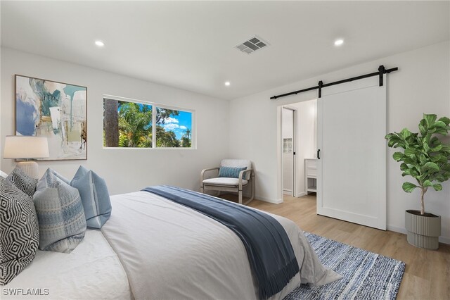 bedroom with connected bathroom, light wood-type flooring, and a barn door