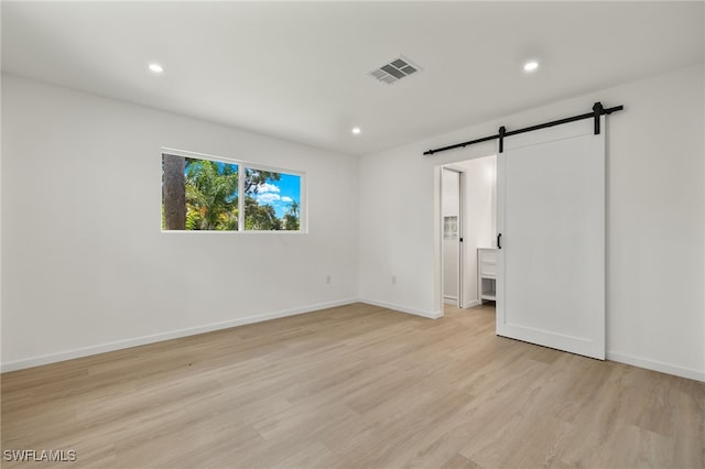 unfurnished bedroom featuring a barn door and light wood-type flooring