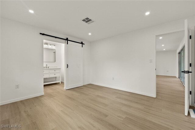 unfurnished bedroom featuring a barn door, sink, connected bathroom, and light hardwood / wood-style floors