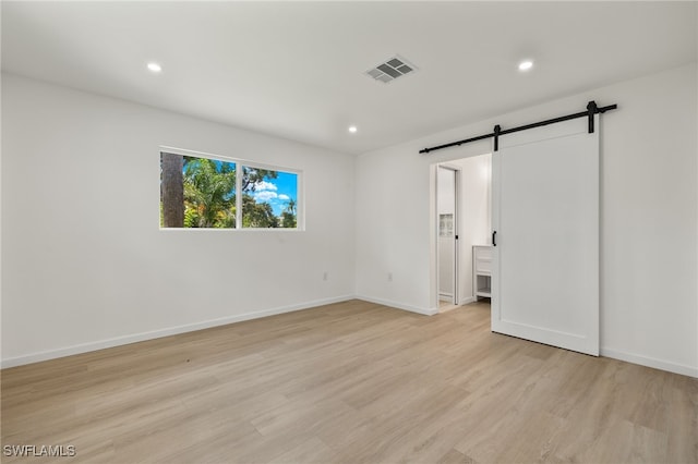 unfurnished bedroom with light wood-type flooring and a barn door