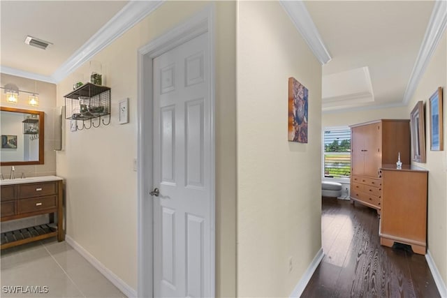 hallway featuring baseboards, visible vents, ornamental molding, wood-type flooring, and a raised ceiling