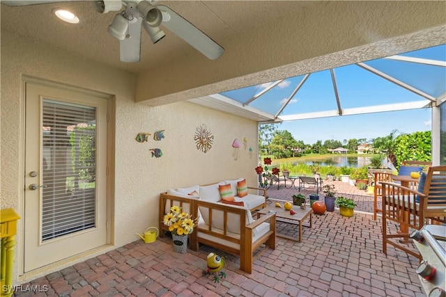 view of patio / terrace with a lanai, a ceiling fan, a water view, and an outdoor living space