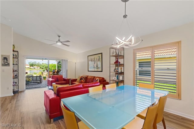 dining area with ceiling fan with notable chandelier, light hardwood / wood-style flooring, and vaulted ceiling