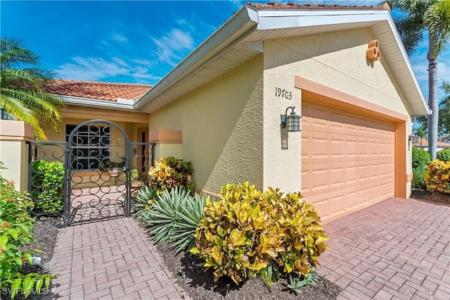 exterior space with a gate, an attached garage, stucco siding, a tiled roof, and decorative driveway