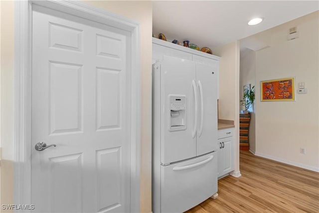 kitchen with white cabinetry, white refrigerator with ice dispenser, and light wood-type flooring