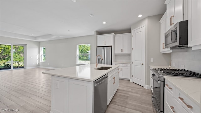 kitchen with stainless steel appliances, white cabinets, an island with sink, sink, and light hardwood / wood-style floors